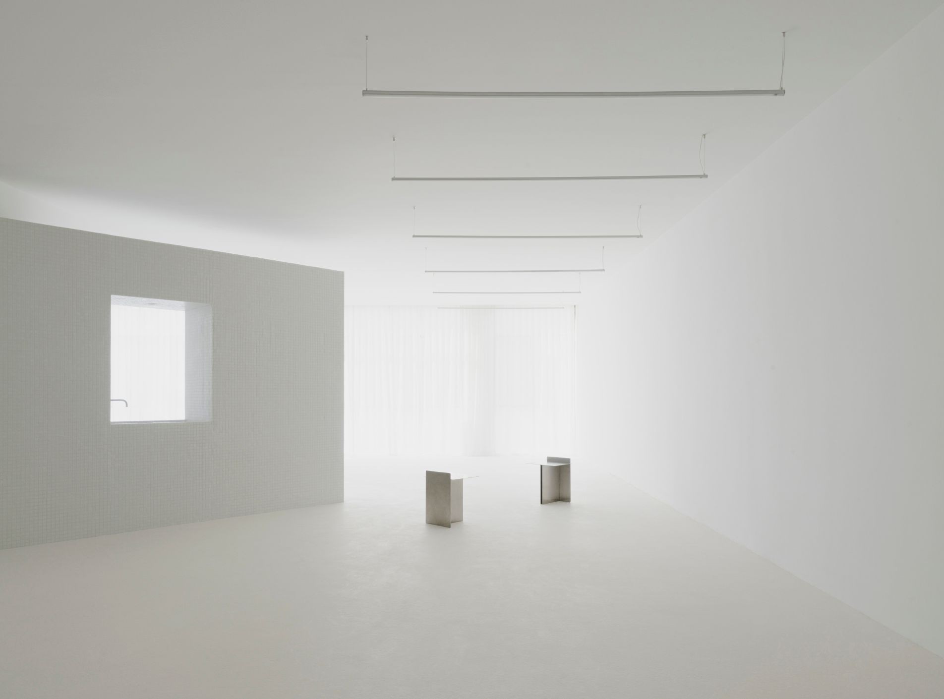 Minimalist white room with two metallic chairs and large window with sheer curtains.