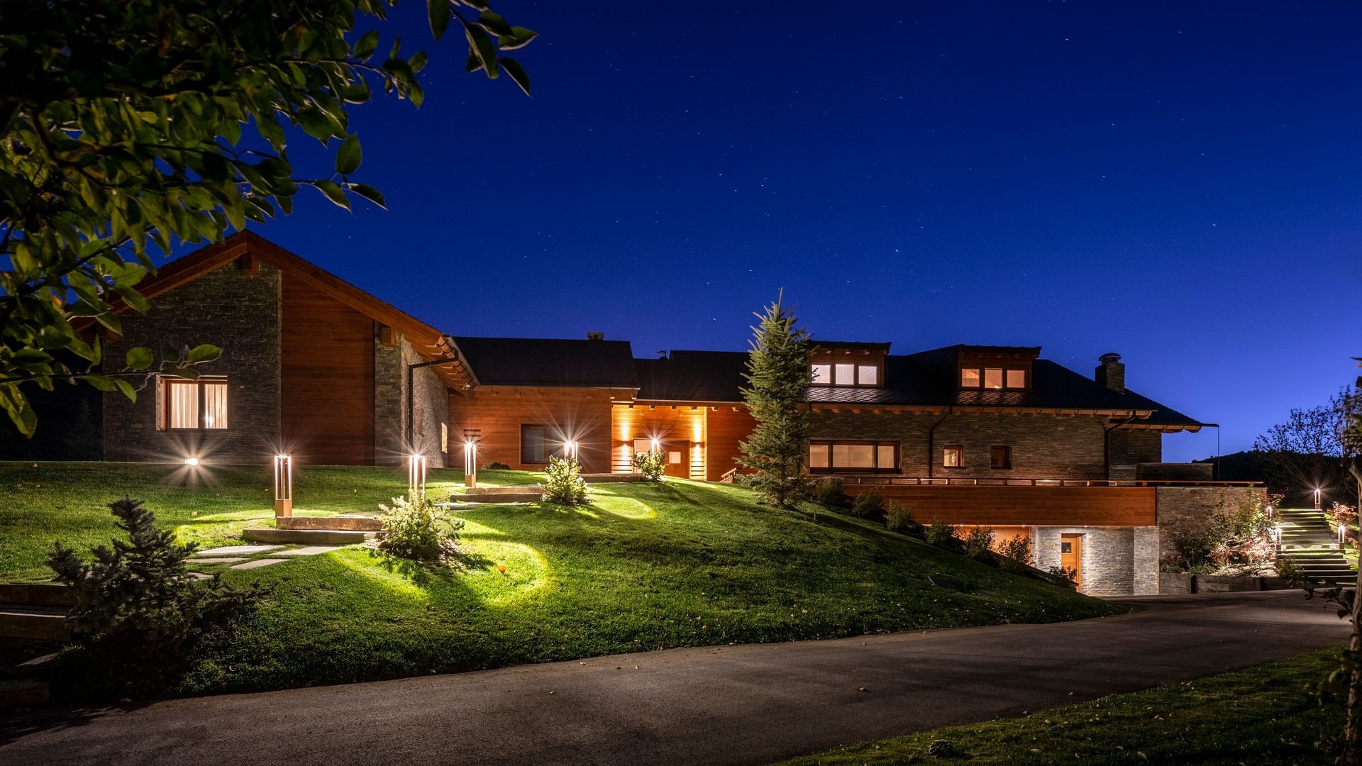 Elegant house with warm exterior lighting, surrounded by greenery and a clear night sky.